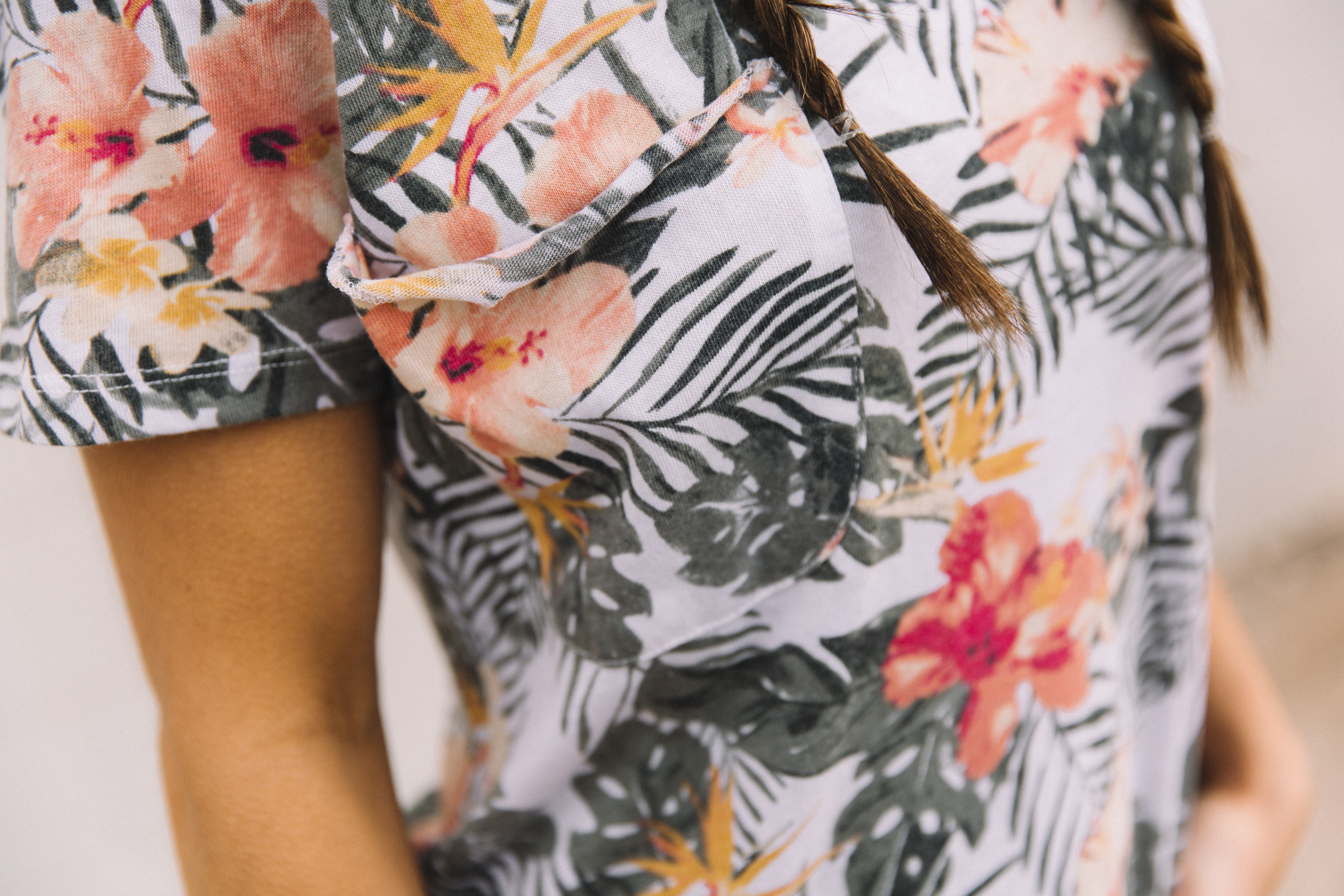 Close up photo of women wearing White Crow's Palm and Hibiscus Floral Tee from the clothing store Buckle.